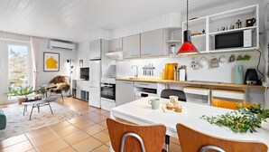 A modern kitchen with white cabinetry, a dining area with a white table and wooden chairs, and a red pendant light above the counter. - Nice home in Fanø with WiFi (Fanø)