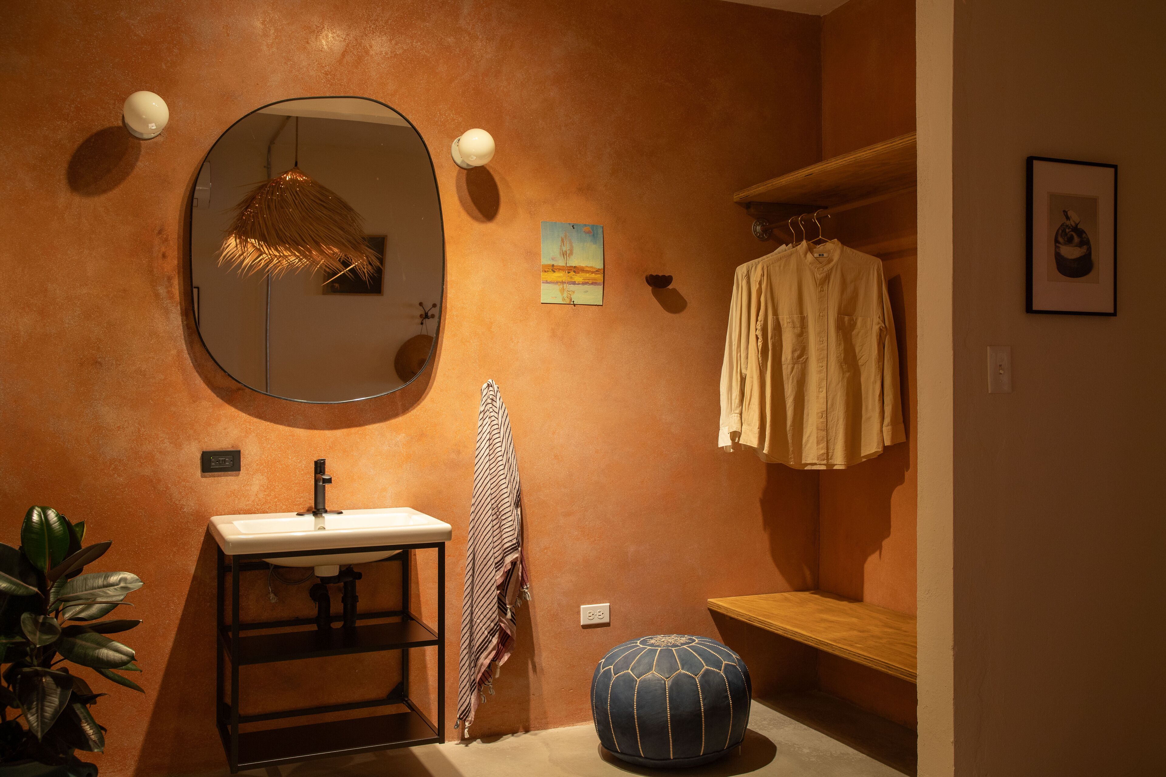 A bathroom with a round mirror, a sink, a towel rack, and a bench.