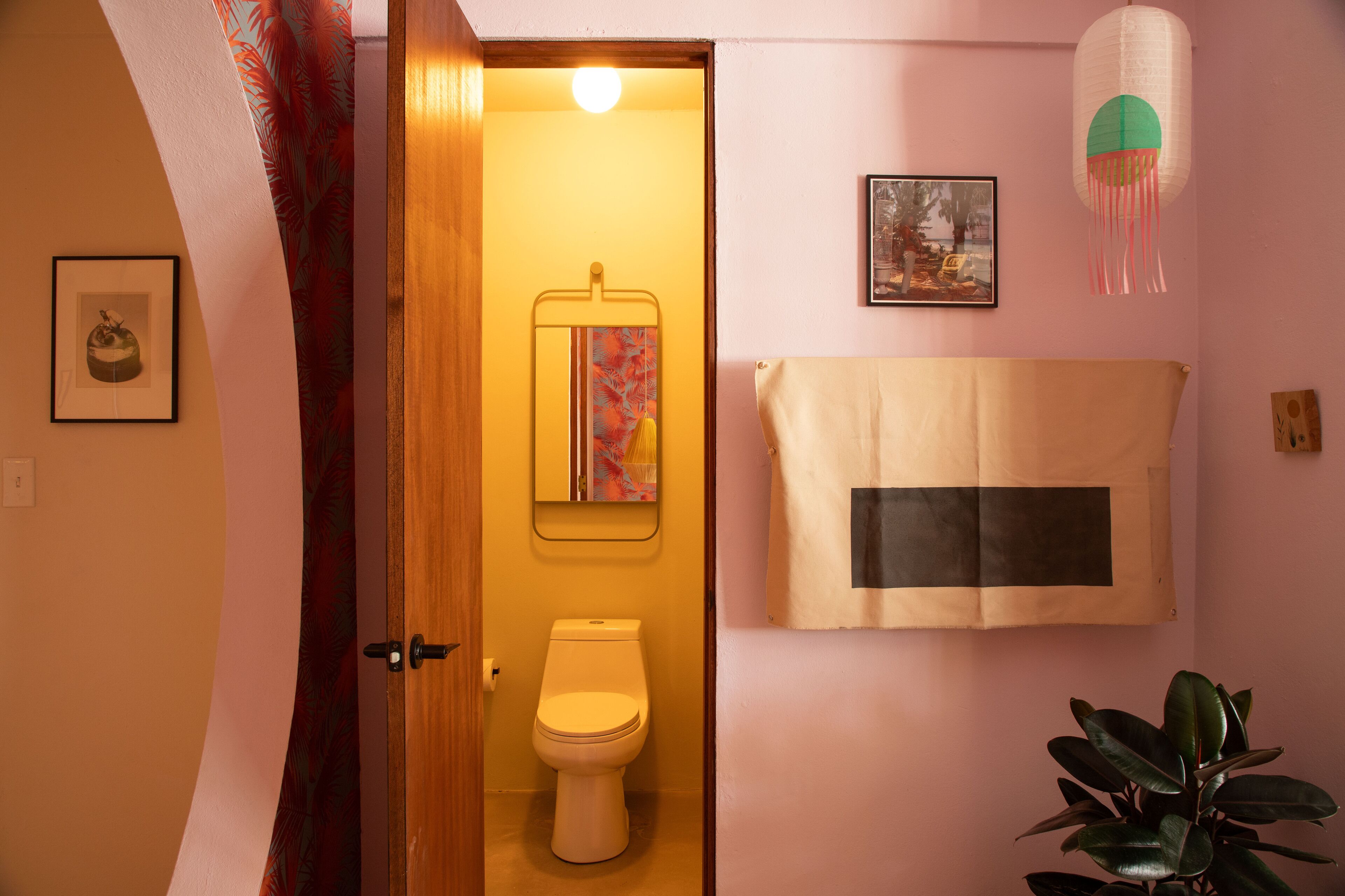 A bathroom with a toilet, a towel hanging on the wall, a framed picture, and a hanging light fixture.