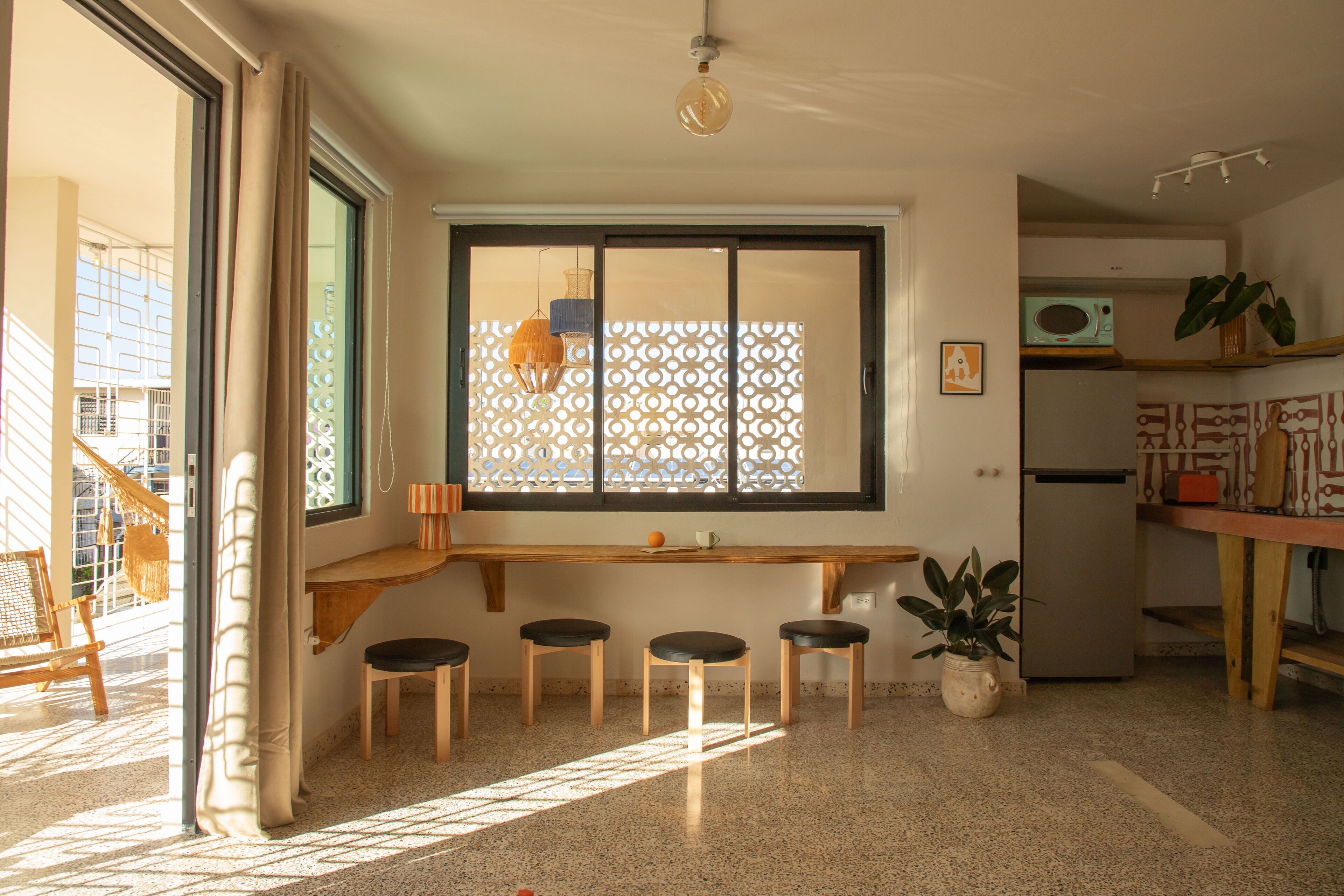 A modern kitchen with a wooden bench, stools, a refrigerator, and a potted plant.