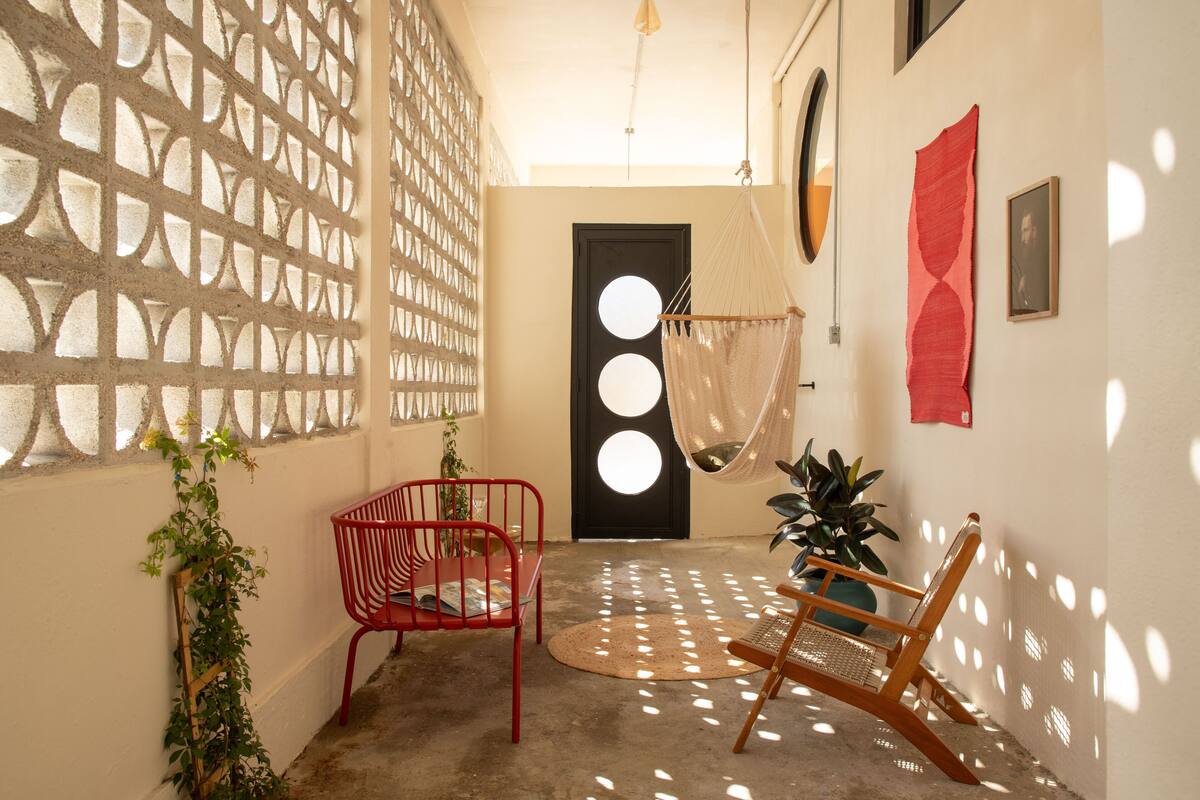 A hallway with a concrete floor, a red chair, a wooden rocking chair, and a black door with circular windows.