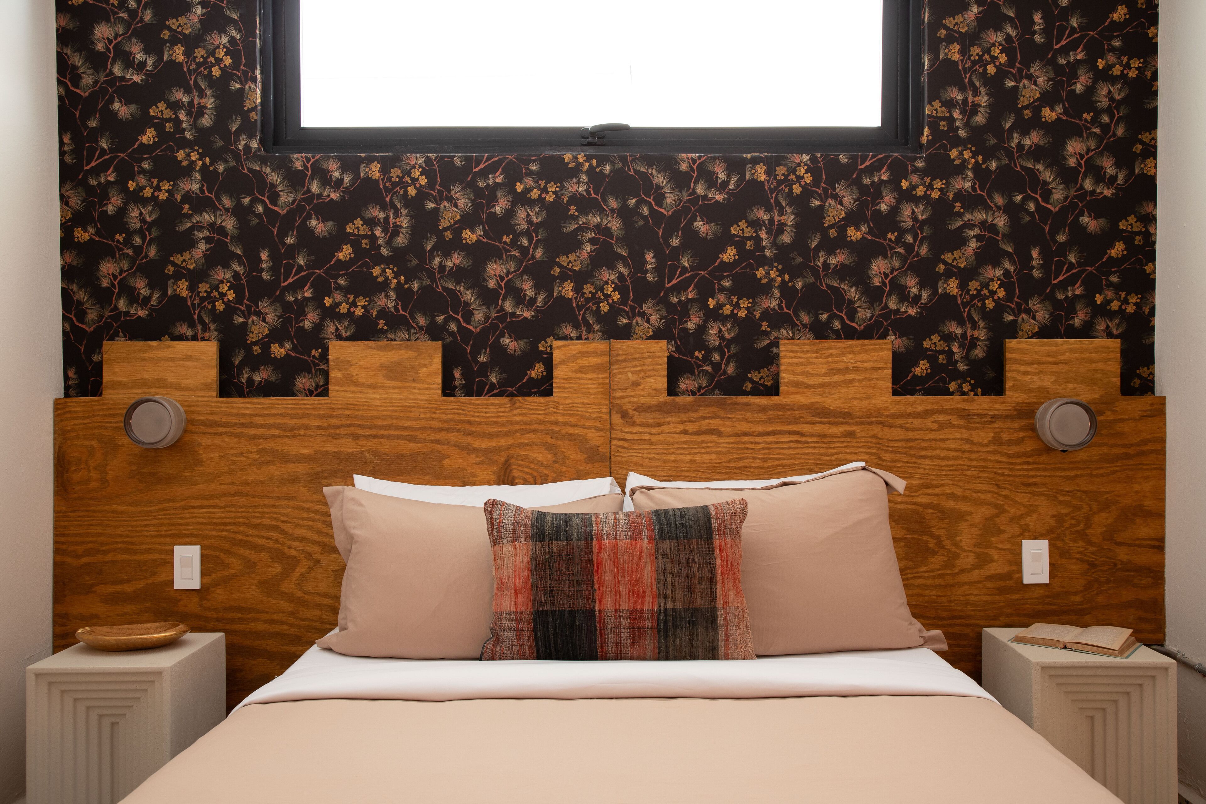 A bedroom with a wooden headboard, two bedside tables, a bed with beige bedding, and a window above.