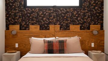 A bedroom with a wooden headboard, two bedside tables, a bed with beige bedding, and a window above.