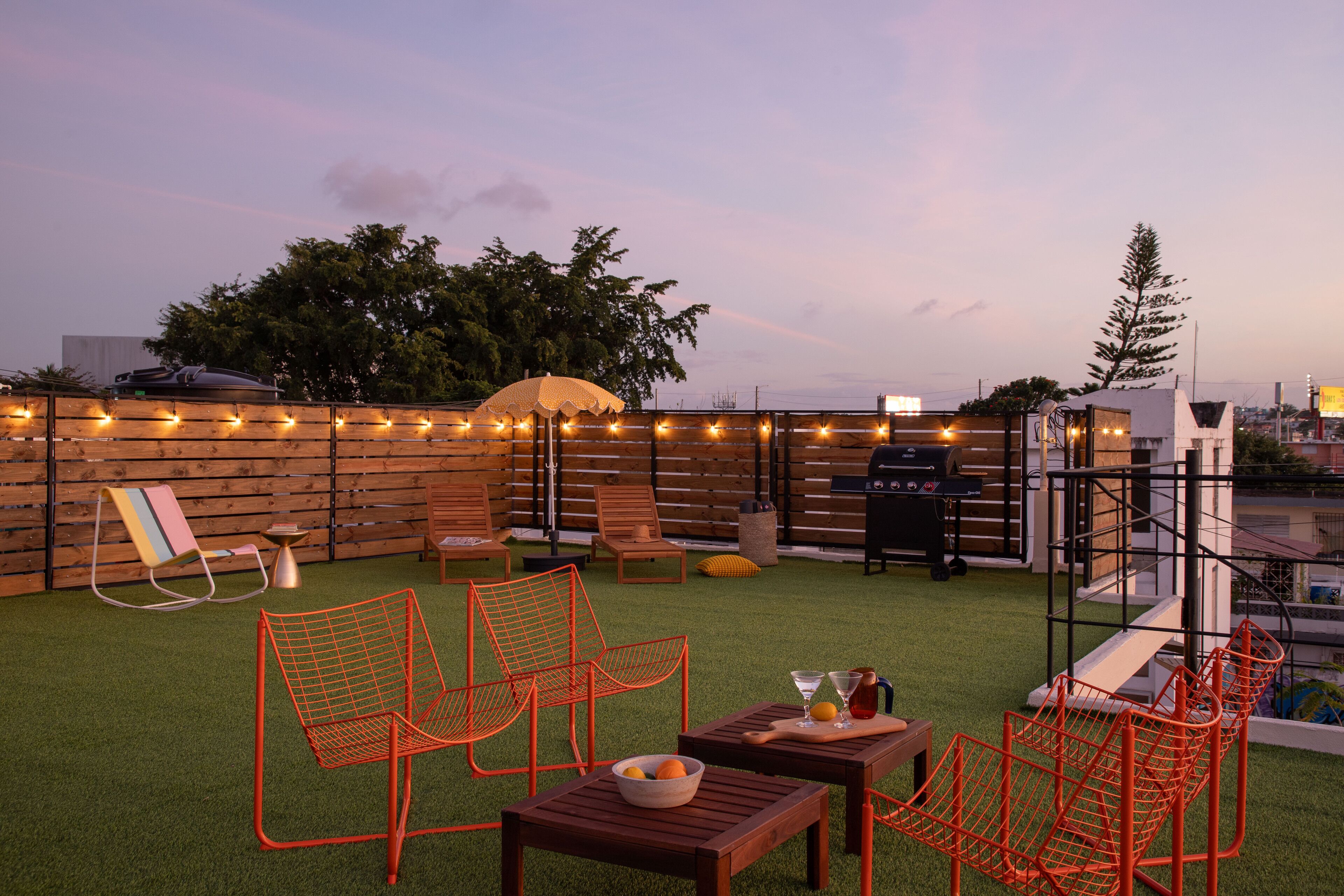 Eine Dachterrasse mit Sitzgelegenheiten im Freien, einem Grill und Lichterketten.