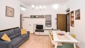 Una sala de estar moderna con un sofá gris, una mesa de comedor con sillas, un televisor y una estantería.