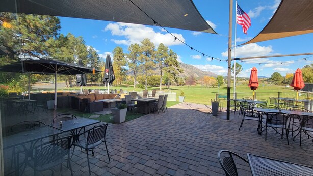 An outdoor patio area with tables and chairs, umbrellas, and a view of a golf course. - Peaceful Flagstaff Condo only minutes to most attractions! (Flagstaff)