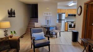 A living room with a sofa, a dining table with two chairs, a kitchen with wooden cabinets and appliances, and a staircase. - Peaceful Flagstaff Condo only minutes to most attractions! (Flagstaff)