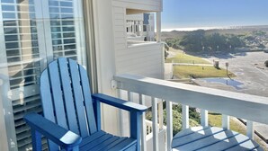 Un balcon avec un fauteuil Adirondack bleu, une balustrade blanche et une vue sur un parking et un paysage lointain.