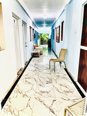 A corridor with a marble floor, a sofa, a chair, and a door on the left.