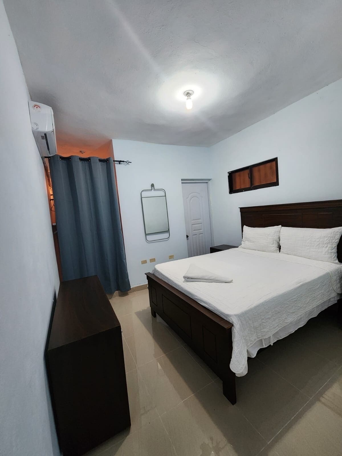 A bedroom with a bed, a bedside table, a mirror, and a ceiling light.