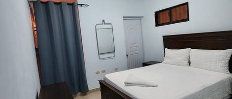 A bedroom with a bed, a bedside table, a mirror, and a ceiling light.