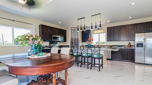 A modern kitchen with dark wooden cabinets, a stainless steel refrigerator, and a central island with bar stools. - Hilo Town Center home (Hilo)