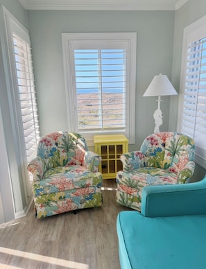 A room with two floral armchairs, a teal sofa, a yellow side table, and a window with blinds. - Rita’s Rejuvenating Oceanfront- Pool- Hot tub- Corner unit-Sleeps 6- APATB  (Atlantic Beach)