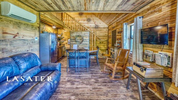 A log cabin interior with a sofa, dining table, chairs, a TV, and a refrigerator.