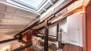 Un interior moderno con tragaluces, vigas de madera y una escalera que lleva a un nivel superior.