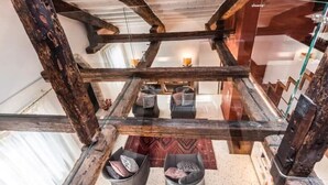 Un interior rústico con vigas de madera a la vista, barandilla de vidrio y un área de descanso con cojines.