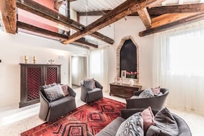 A spacious living room with exposed wooden beams, a red patterned rug, and a fireplace.