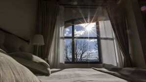 A bedroom with a large window, a bed, and a bedside lamp.
