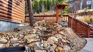 Una cascada de piedra que se precipita sobre rocas hacia un estanque, rodeada por una terraza de madera y un edificio de madera.