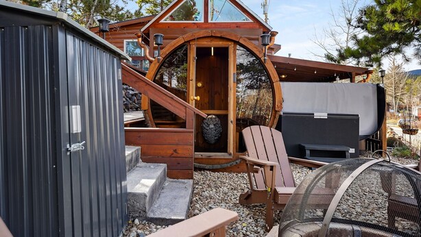 Una cabaña con fachada de madera, una puerta circular grande y un pequeño porche con una silla y una parrilla.