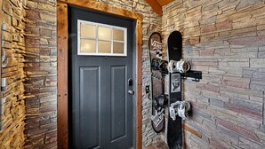 Una pared de piedra con una puerta negra, una ventana y un perchero adosado a la pared que sostiene una tabla de snowboard y esquíes.