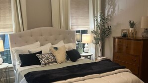 A bedroom with a large bed, a nightstand, a dresser, and a window with curtains. - Charming Pine Cottage near SFA, azalea gardens,  & walking trails. (Nacogdoches)