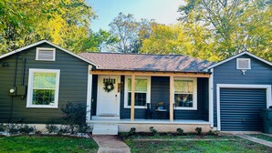 A two-story house with a front porch, a garage, and a small garden area. - Charming Pine Cottage near SFA, azalea gardens,  & walking trails. (Nacogdoches)