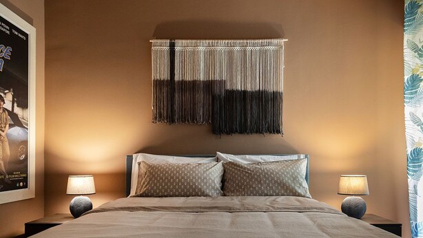 Un lit bien fait avec deux oreillers, une décoration en macramé accrochée au mur et deux lampes de chevet.