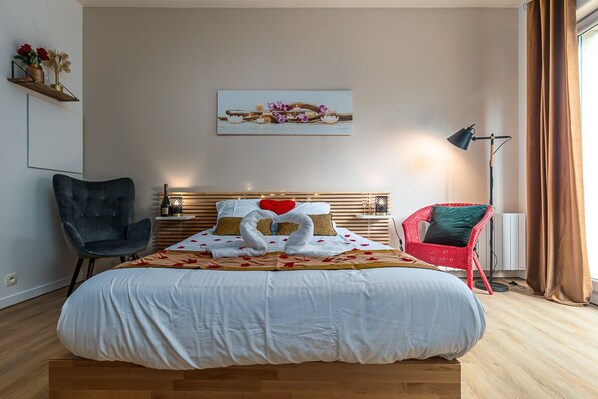 A bedroom with a large bed, a wooden headboard, a red chair, a black chair, a floor lamp, and a painting on the wall. - Havre de Paix  Jacuzzi (Asnieres-sur-Seine)