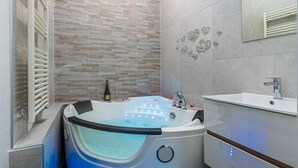 A modern bathroom with a large bathtub, a vanity with a mirror, and a tiled wall with heart patterns. - Havre de Paix  Jacuzzi (Asnieres-sur-Seine)