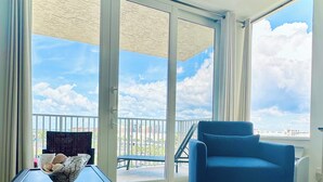 Ein Zimmer mit einer großen Schiebeglasdoor zum Balkon, ein blauer Sessel und ein kleiner Tisch mit einer dekorativen Schale.