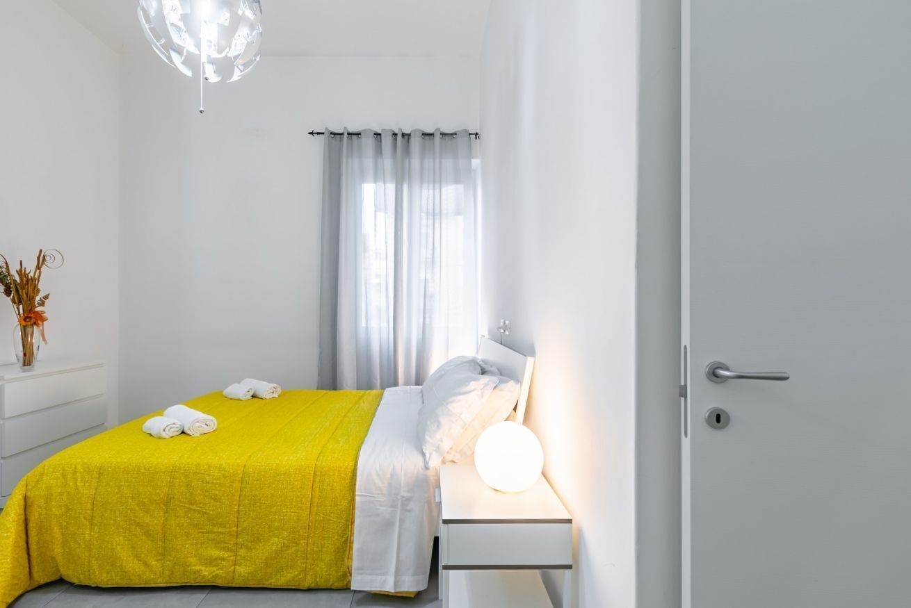 A modern bedroom with a yellow bedspread, a bedside lamp, and a white nightstand.