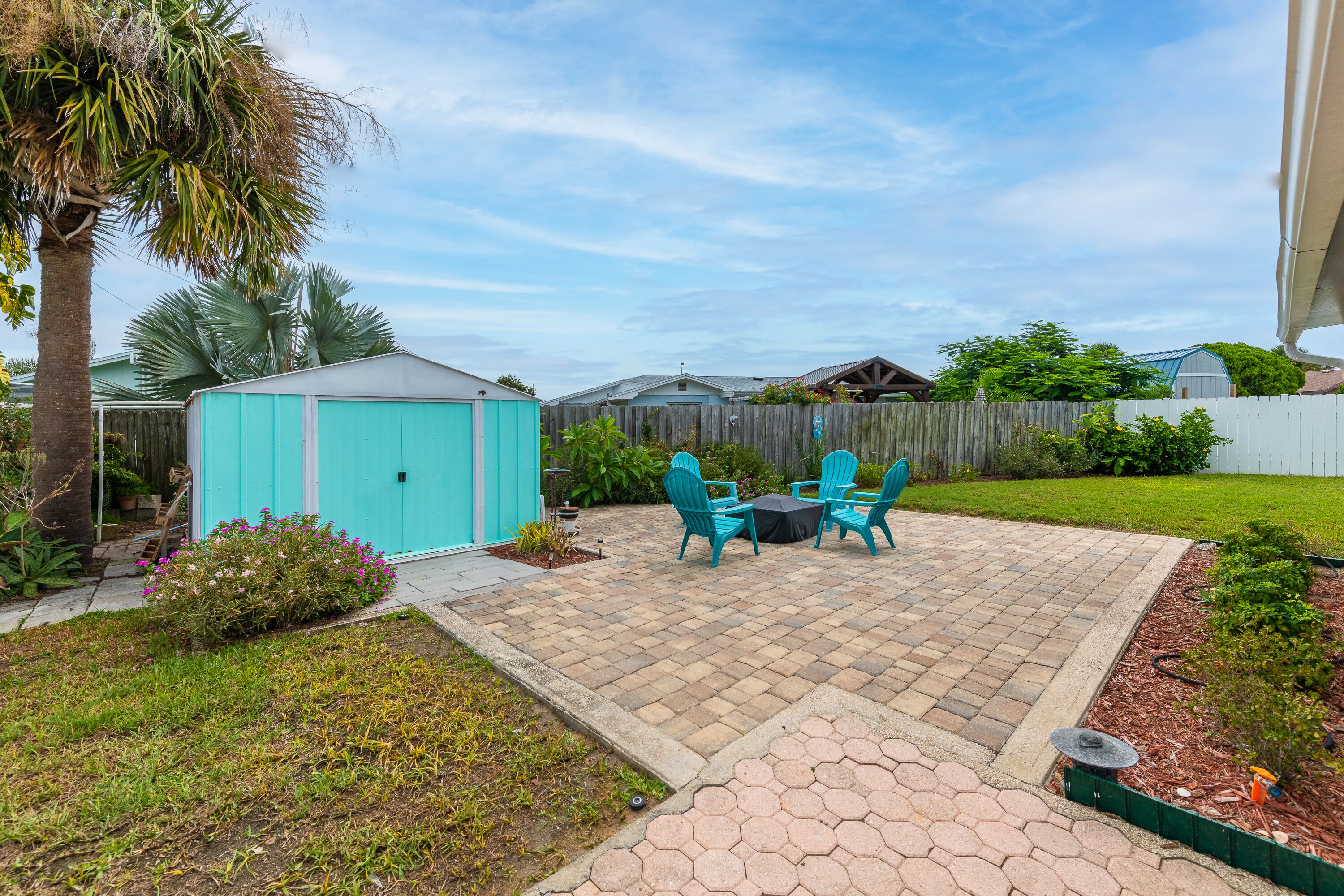 A backyard patio with a wooden fence, a blue shed, and a small garden area.