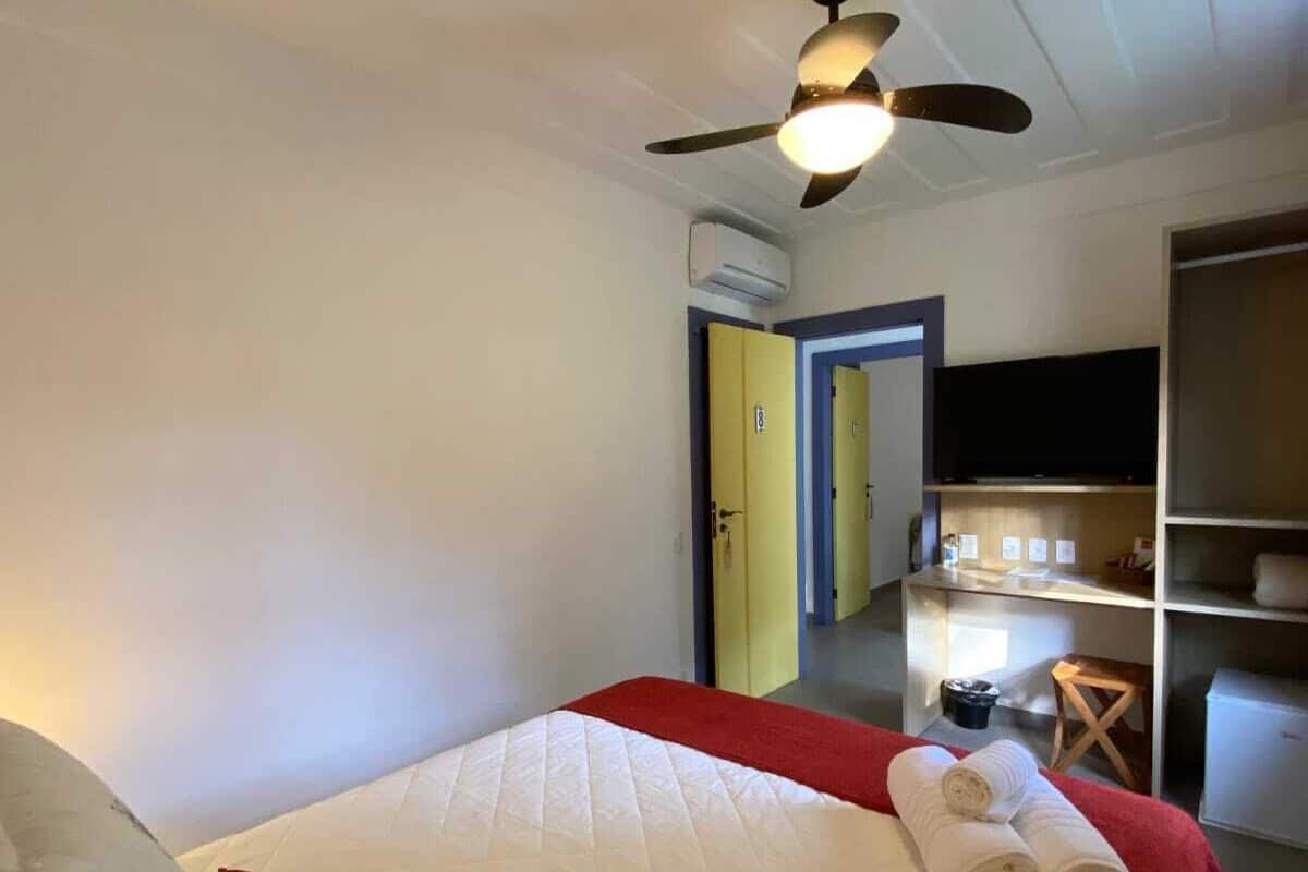 A hotel room with a bed, a ceiling fan, a desk with a chair, and a television.