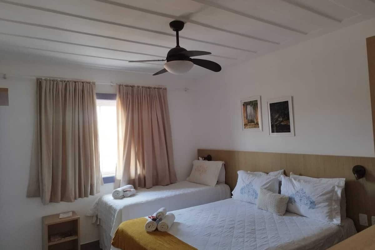 A hotel room with two beds, a ceiling fan, and a window with curtains.