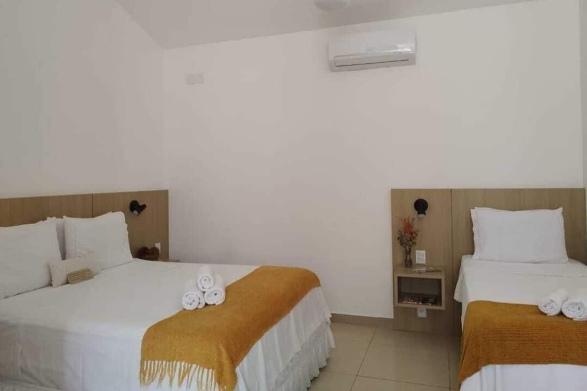 A hotel room with two beds, a ceiling fan, an air conditioning unit, and a small bedside table with a vase of flowers.