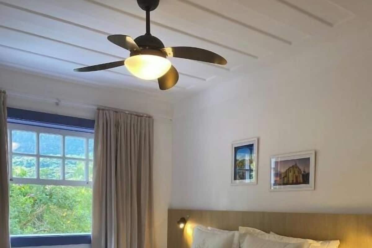 A neatly made bed with a brown throw blanket, a ceiling fan, and two framed pictures on the wall.