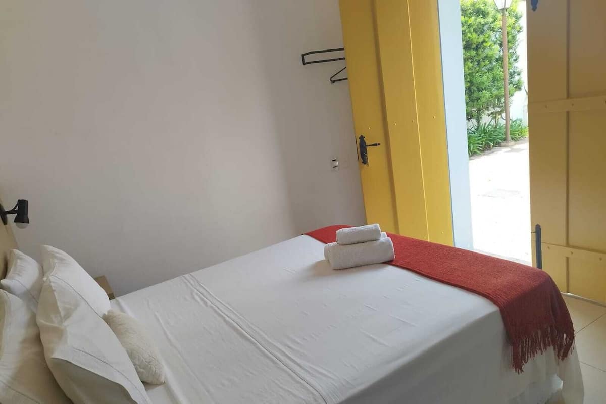 A single bed with white bedding, a red throw blanket, and two folded white towels.