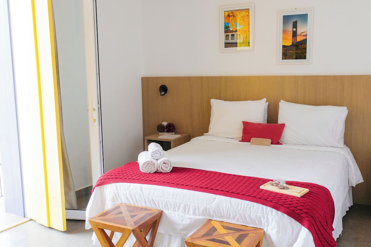 A hotel room with a large bed, a wooden headboard, a nightstand with a lamp, and two framed pictures on the wall.