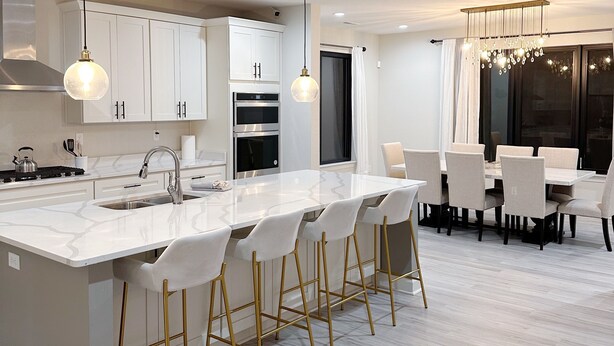 A modern kitchen with white cabinetry, a central island with bar stools, and a dining area with a chandelier. - Embrace Tranquility: A modern retreat home where serenity meets style (Elizabeth City)