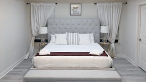 A bedroom with a large bed, a chandelier, and curtains. - Embrace Tranquility: A modern retreat home where serenity meets style (Elizabeth City)
