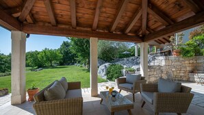 Une terrasse extérieure avec des meubles en osier, un mur en pierre et une vue sur un paysage verdoyant.