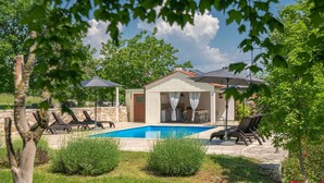 Un espace aménagé au bord de la piscine, comprenant un coin salon couvert, des chaises longues et un mur en pierre.