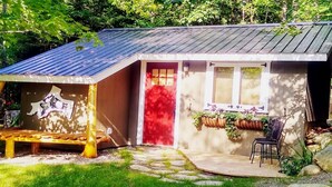 Uma casa pequena com uma porta vermelha, um banco e uma cadeira na parte externa.