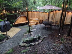 A wooden deck with a built-in bench, a table with chairs, and string lights. - Osprey Cabin at Walker Pond by Vermont Tree Cabin (Newport)