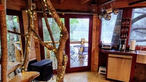 A rustic cabin interior with a wooden staircase, a fireplace, a kitchen area, and a view of the outdoors. - Vermont Tree Cabin on Walker Pond, private retreat (Newport)