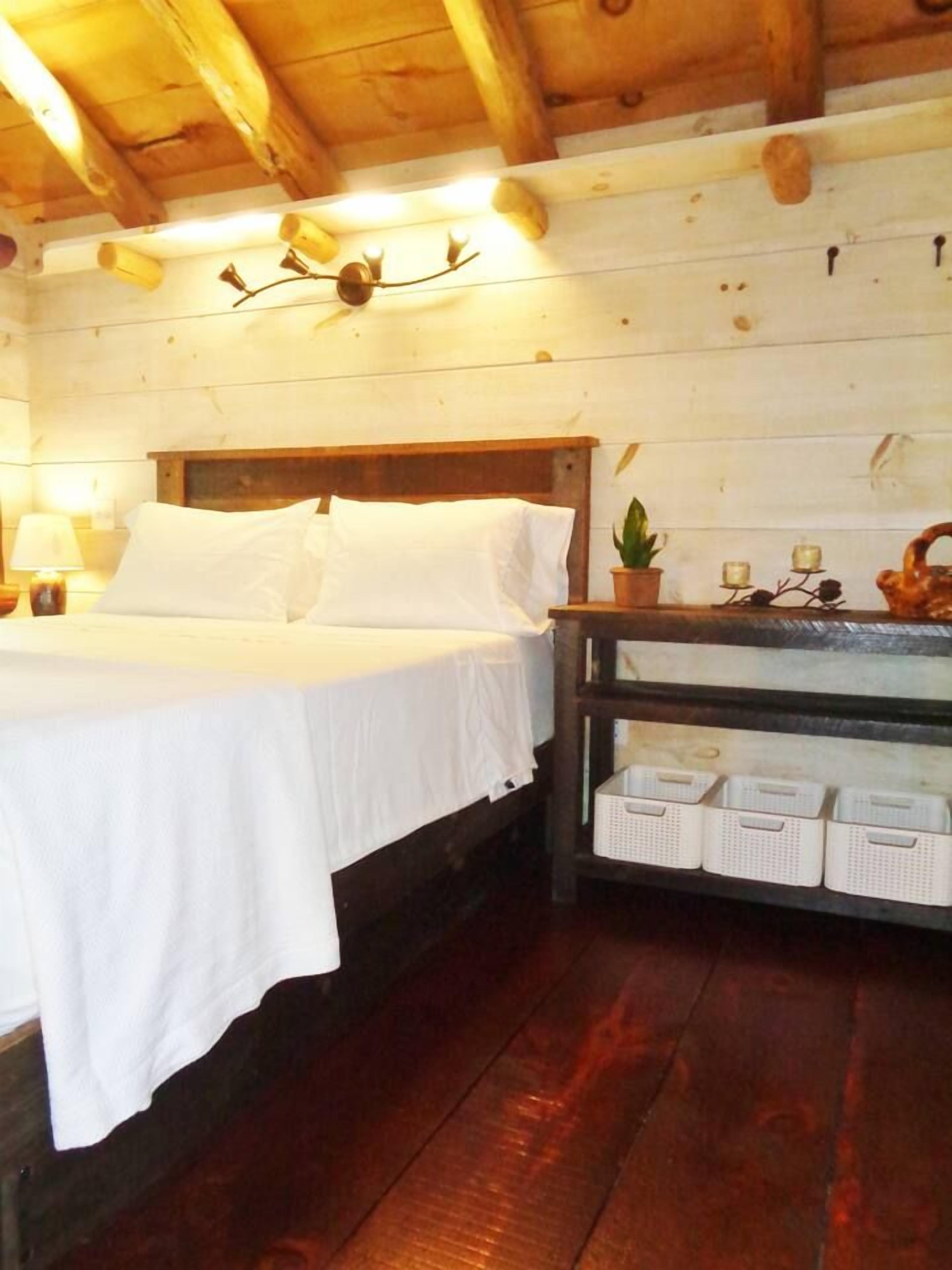 Een houten kamer in chaletstijl met een bed, een nachtkastje met lamp en een plank met opbergmanden.