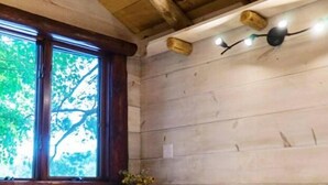 A wooden cabin bedroom with a bed, a nightstand, a window, and a wall-mounted light fixture. - Vermont Tree Cabin on Walker Pond, private retreat (Newport)