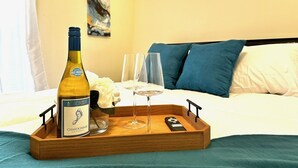 Quarto de hotel com uma cama, uma bandeja de madeira com uma garrafa de Chardonnay, dois copos e um controle remoto.