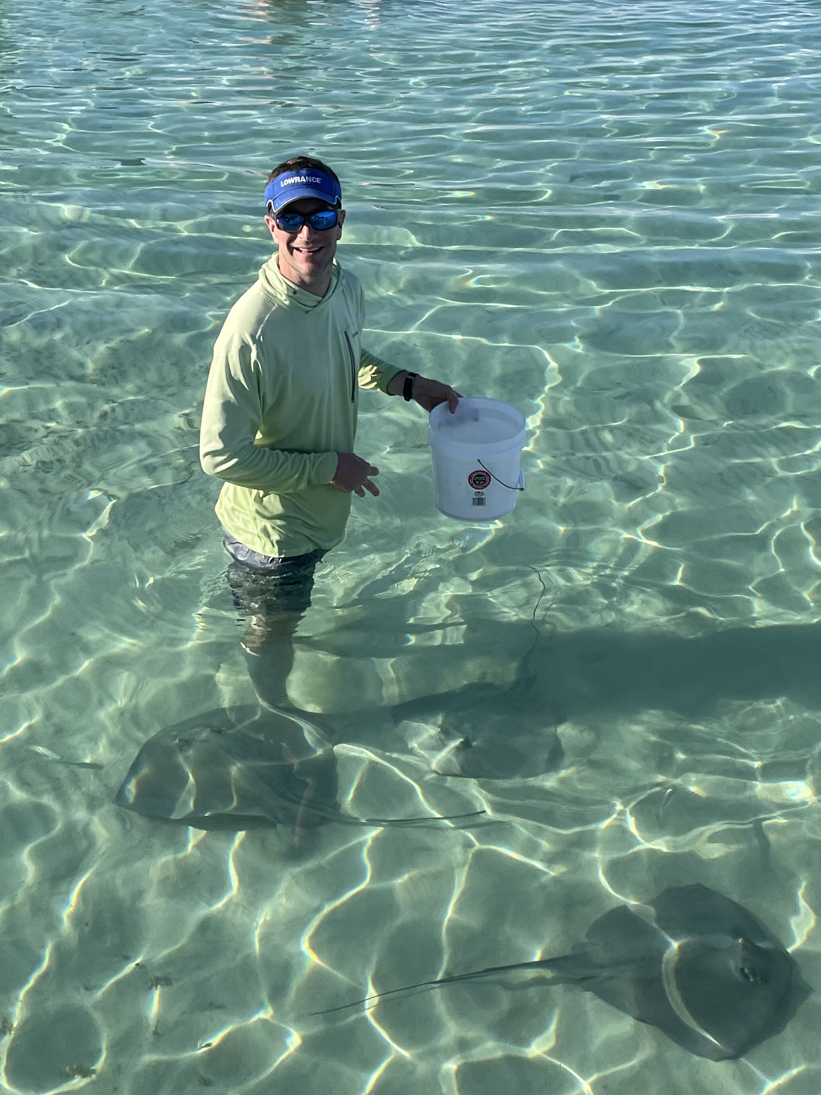 Una persona de pie en aguas claras y poco profundas, sosteniendo un cubo blanco.